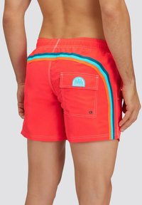 Shorts da nuoto rossi con strisce laterali multicolori, vita elastica e tasca posteriore con una patch blu. Tessuto a superficie liscia.