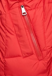 Rode pufferjack met een zijzak met een zilveren rits en textiel met structuur. Glad, geïsoleerd materiaal met gestikte details.