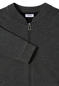 Giacca grigia scura con zip, texture a spina di pesce, scollatura tonda e una sola manica visibile. L'etichetta del marchio riporta "CECiL."