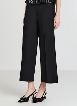 Pantalon noir à jambes larges en tissu lisse avec une finition polie. Associé à des talons slingback noirs ornés de détails à volants.