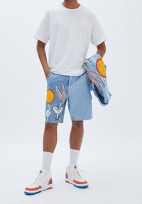 Pantalones cortos de mezclilla en azul claro con un gráfico de Bugs Bunny, combinados con una camiseta blanca lisa y zapatillas altas en blanco con detalles en naranja.