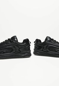 Schwarze Sneakers aus glattem Synthetikmaterial, mit niedrigem Design, strukturierten Akzenten und dicken schwarzen Gummisohlen.