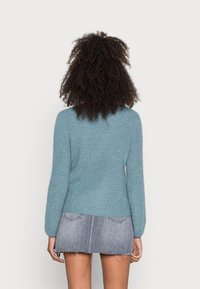 Himmelblaues, strukturiertes Sweatshirt mit einer taillierten Passform und langen Ärmeln, kombiniert mit einem grauen Denim-Minirock mit fransigem Saum und Gesäßtaschen.