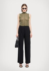 Haut sans manches vert olive avec un col montant, associé à un pantalon cargo noir à pattes larges avec poches avant. Les accessoires incluent un sac à main noir et des lunettes de soleil.