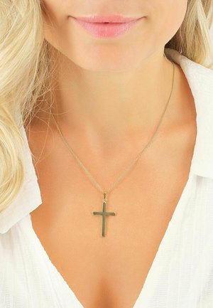 Femme portant un collier avec pendentif croix en or sur un chemisier blanc, montrant le décolleté ainsi qu'une partie de ses lèvres et de ses cheveux blonds.