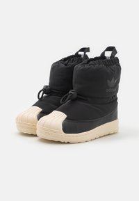 Černé izolované boty s kulatou béžovou gumovou špičkou, elastickým lemem nahoře a nastavitelným stahovacím šňůrkem. Mají prošívané detaily a logo.