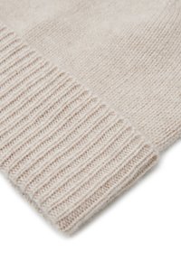 Tessuto lavorato a maglia beige con una trama liscia. Presenta un polsino a coste e una sezione a maglia piatta. Materiale morbido e leggero, ideale per il layering.