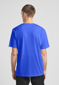 T-shirt bleu à manches courtes en tissu lisse, avec un col rond et une coupe décontractée. Le dos est uni, sans graphismes ni motifs.