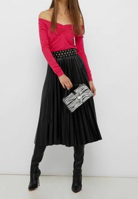 Top rosa off-the-shoulder, gonna nera plissettata con cintura, stivali neri al ginocchio e una borsa a tracolla a stampa zebra. Texture morbide e colori a contrasto.