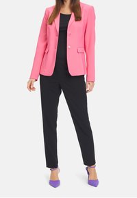 Rosa blazer med två knappar och framfickor, kombinerad med svarta byxor. Modellen bär lila högklackade skor. Konturerad passform och slät textur.