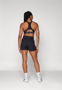 Top cropped atlético preto com um design de costas nadador, emparelhado com calções justos pretos com tecido texturizado e uma cintura franzida.