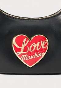 Schwarze Ledertasche mit goldfarbenem Reißverschluss, auf der Vorderseite mit einem roten Herzemblem und goldfarbenem "Love Moschino"-Schriftzug versehen.