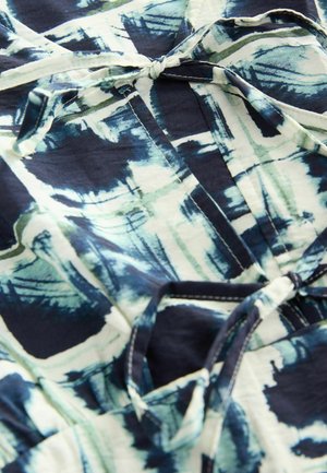 Zračna bluzica iztvorena iz tkanine z morsko modrim, zelenim in belim abstraktnim vzorcem. Ima zapiranje na zavezo in vidno šivanje na robovih.