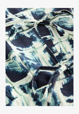 Top de tela fluida con un patrón abstracto en navy, verde y blanco. Presenta un cierre con lazo y costuras visibles en los bordes.