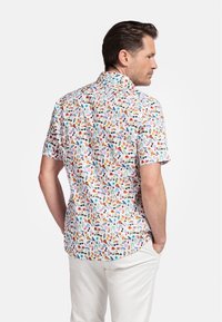 Chemise à manches courtes avec un fond blanc ornée d'un motif coloré et ludique de fleurs, d'oiseaux et d'autres motifs. Col à boutons.
