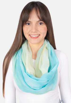 Young woman with long brown hair wearing a white top and a blue and green gradient scarf, smiling against a plain light background.