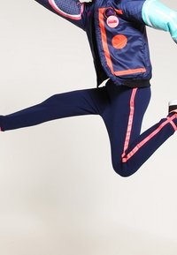 Navy athletic leggings with pink side stripes, paired with a navy jacket featuring colorful circular accents and a textured sleeve.