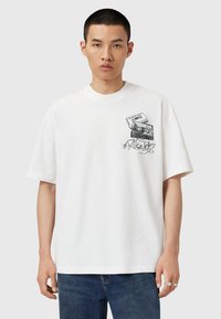 Tricou alb din bumbac cu un grafic ce reprezintă o cameră și o casetă audio, cu contururi negre și text cursiv pe partea din față. Mâneci scurte, croială lejeră.