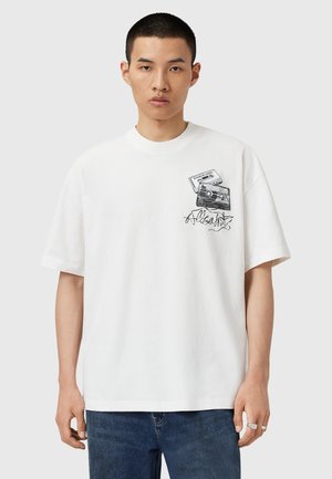 Hvid bomulds t-shirt med et grafik af et kamera og et kassettebånd, med sorte omrids og kursiv tekst på forsiden. Korte ærmer, afslappet pasform.