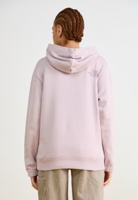 Felpa rosa chiaro realizzata in tessuto morbido con cappuccio a doppio strato. Presenta un logo discreto sulla parte superiore della schiena e una vestibilità comoda.