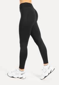 Leggings nere con una fascia alta in vita, realizzate in materiale liscio ed elastico. Abbinate a sneaker bianche con dettagli grigi.