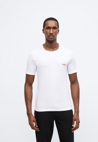 Balta trumpomis rankovėmis marškinėliai iš lygaus audinio. Turi apvalų kaklo iškirpimą ir raudoną „HUGO“ logotipą kairėje krūtinės pusėje. Paprastas ir prigludęs dizainas.