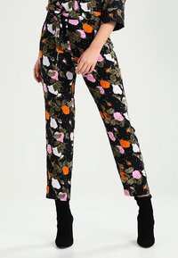 Pantalons floraux avec un fond noir, ornés de roses roses, oranges et blanches, de feuilles vertes, et d'une coupe ajustée.