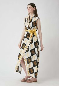 Sleeveless wrap dress with a yellow tie belt, featuring black and white patterned fabric with orange floral designs, and a side slit.