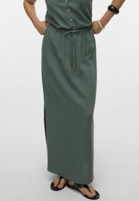 Longue jupe maxi verte en matériau doux, dotée d'une taille élastique et d'un cordon de serrage avec des perles en bois, fentes latérales pour plus de confort.