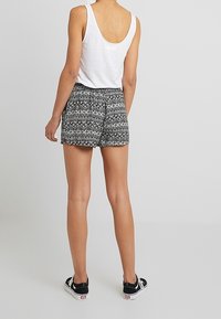 Černo-bílé šortky s geometrickým vzorem, vyrobené z lehkého materiálu, v kombinaci s bílým bezrukávovým topem a černými botami.