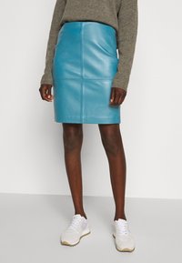 Blauwe leren kokerrok met een aansluitende silhouette, met een gepaneeld ontwerp en een gladde textuur. Gepaard met witte sportschoenen.