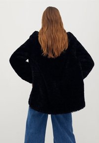 Zwarte nepbontjas met een losse pasvorm, wijde mouwen en een gestructureerd oppervlak, gecombineerd met lichtblauwe wijde spijkerbroek.