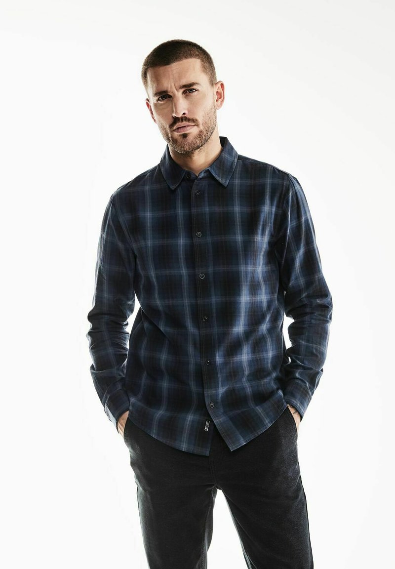 Camicia a maniche lunghe a scacchi in blu scuro e nero, realizzata in tessuto morbido. Presenta un colletto button-down e chiusura frontale con bottoni.