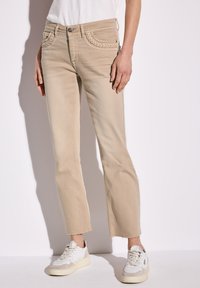 Beige denim farkut, joissa on punottu taskusuunnittelu, suora leikkaus, revitty helma, yhdistettynä valkoisiin ja harmaisiin lenkkareihin.
