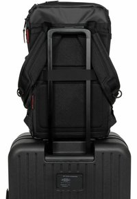 Black fabric backpack with mesh padding, attached to a black hard-shell suitcase with vertical grooves and a metal handle.