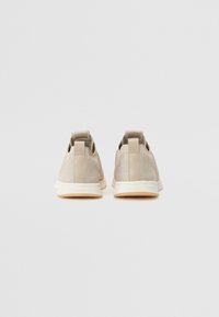 Beige Sneaker mit einem strukturierten Mesh-Obermaterial und flachen Zuglaschen. Die Sohle ist cremefarben mit einer Gummi-Oberfläche. Minimalistisches Design.
