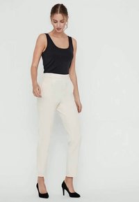 Hvite skräddersydde bukser med en glatt tekstur, parret med en tettsittende svart tank topp og svarte høye hæler. Outfiten har et minimalistisk design.