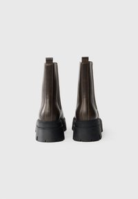 Rudos odinės Chelsea botai su storesne juoda guma, išsiskiriantys ryškiais šoninių siūlių raštais ir traukimo kilpomis nugaroje, kad būtų lengva užsidėti.