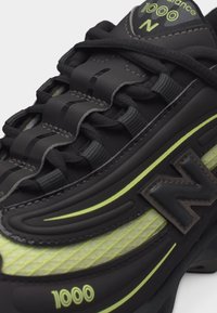Μαύρο και νέον πράσινο sneaker New Balance 1000 με λεπτομερή κορδόνια, υφασμάτινα πάνελ με υφή και έντονο λογότυπο "N" στο πλάι.