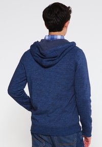 Mörkblå huoodie i strukturerad stickad tyg. Har en avslappnad passform, ribbade ärmslut och luva med dragsko.