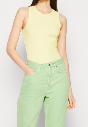 Yellow ribbed tank top with a round neckline, paired with high-waisted green denim jeans. The jeans have side pockets and a slightly faded texture.