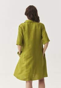 Rochie verde din in cu un croi lejer, mâneci scurte răsucite și buzunare laterale, având guler și o fustă până la genunchi.