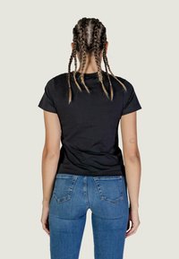 T-shirt nera a maniche corte, design aderente, abbinata a jeans in denim blu. Il T-shirt presenta un collo pulito e una texture liscia.