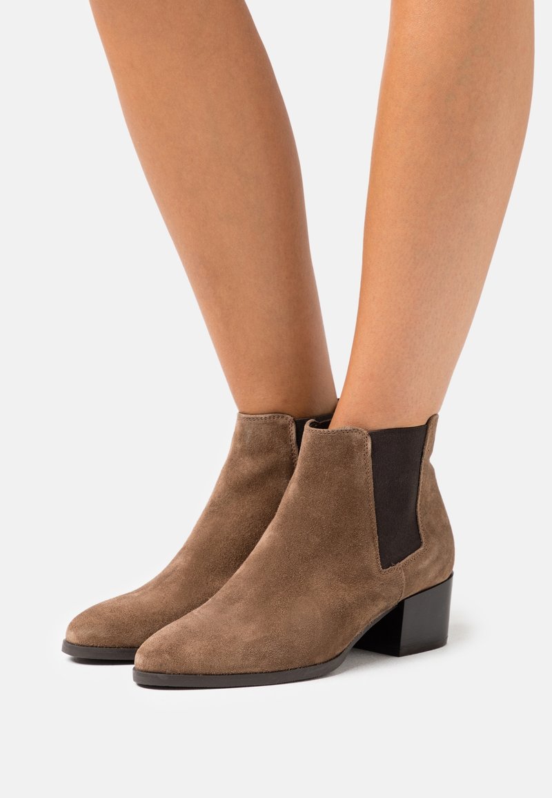 Botas de tobillo de ante marrón con punta afilada, paneles laterales elásticos y un tacón bajo cuadrado. Textura suave con detalles de costura sutiles.