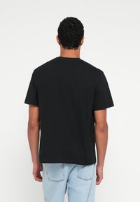 Melna kokvilnas T-krekls ar apaļu apkakli, īsām piedurknēm un brīvu piegriezumu, ar vienkāršu muguru bez rotājumiem.