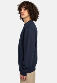 Sudadera de algodón azul marino con mangas largas, puños acanalados, cuello redondo y diseño impreso en la parte posterior. Textura suave, corte relajado.