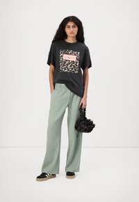 Black t-shirt with a leopard print square and "L'amour" text, paired with light green wide-leg trousers and a black floral drawstring bag.