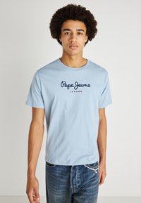 Ανοιχτό μπλε βαμβακερό μπλουζάκι με κοντά μανίκια, στρογγυλή λαιμόκοψη, με το λογότυπο "Pepe Jeans London" σε ναυτικό μπλε σκριπτ με κόκκινες λεπτομέρειες.