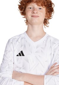 Witte lange mouwen trui met een getextureerd geometrisch patroon en V-hals ontwerp. Met een zwart adidas-logo op de linkerkant van de borst.