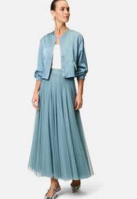 Helles blauer Satin-Bomberjacke mit elastischen Bündchen, kombiniert mit einem fließenden hellblauen Tüllrock. Silberne High-Heels runden das Outfit ab.